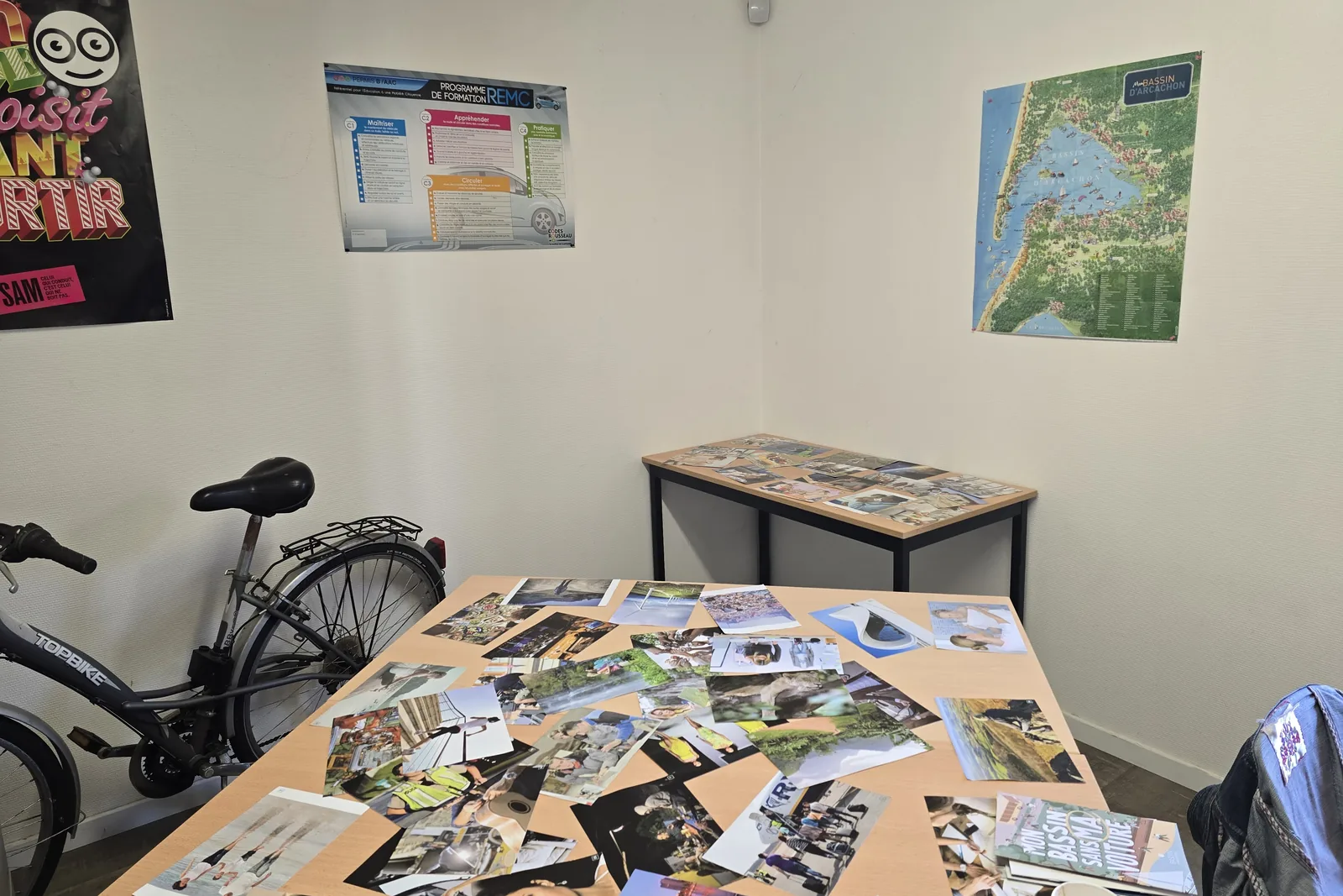 Salle préparée pour un atelier : des photos de mobilité étalées sur une table, un vélo et une carte du Bassin au mur.