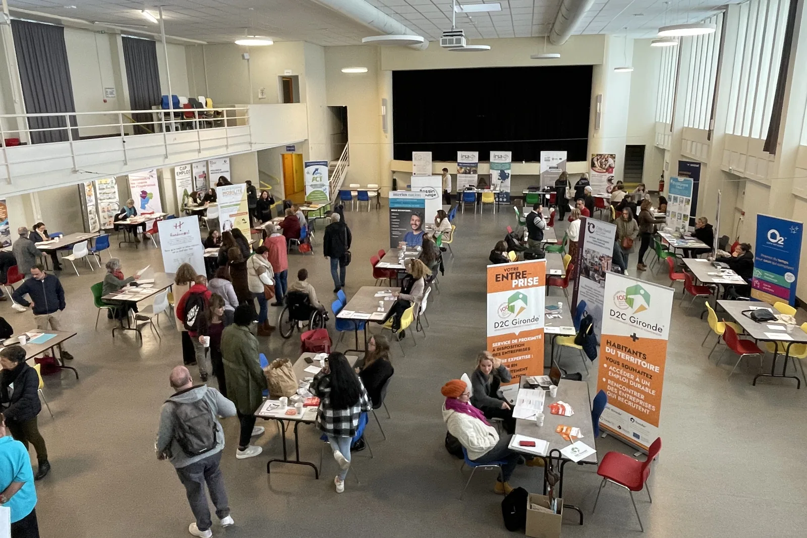 Forum emploi et handicap vu d’en haut : des visiteurs, dont une personne en fauteuil roulant, rencontrent des structures à leurs stands.