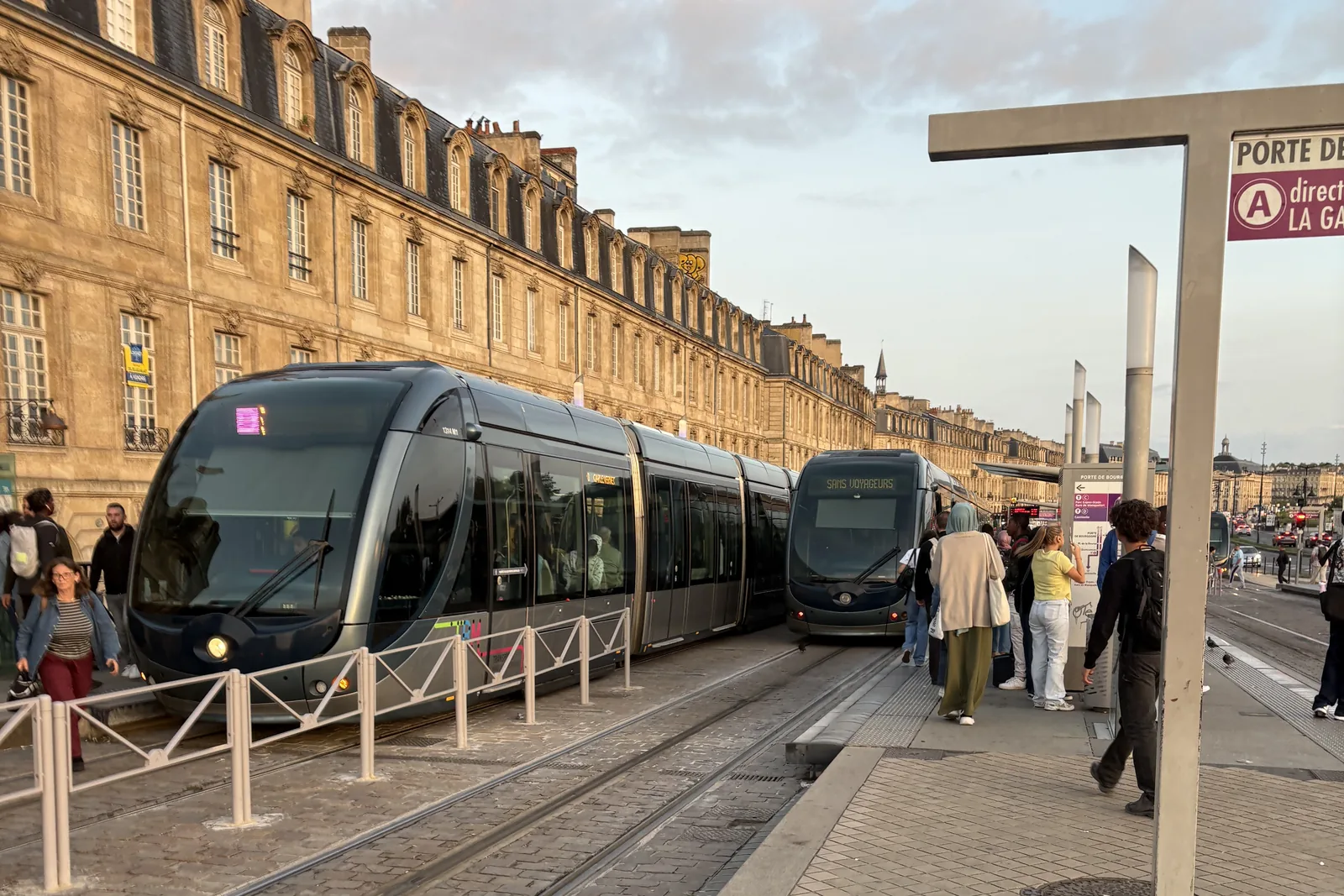 Un tramway à l’arrêt, le long d’un quai pavé et d’une longue façade en pierre.