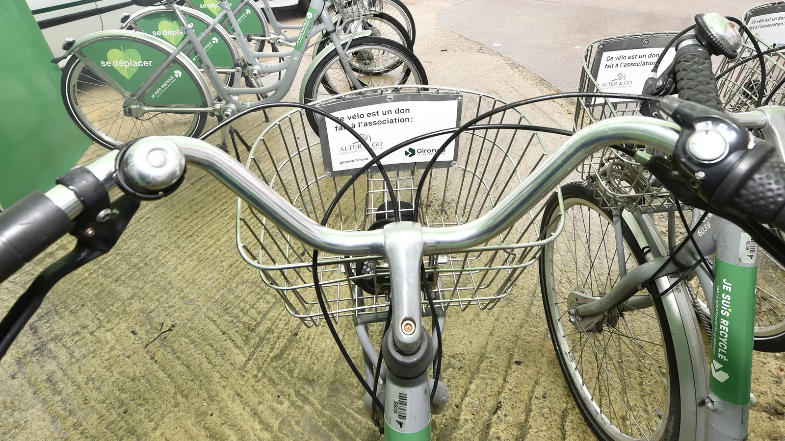 Des vélos prêtés par la plateforme mobilité, garés côte à côte ; une étiquette indique que le vélo est un don fait à l'association.